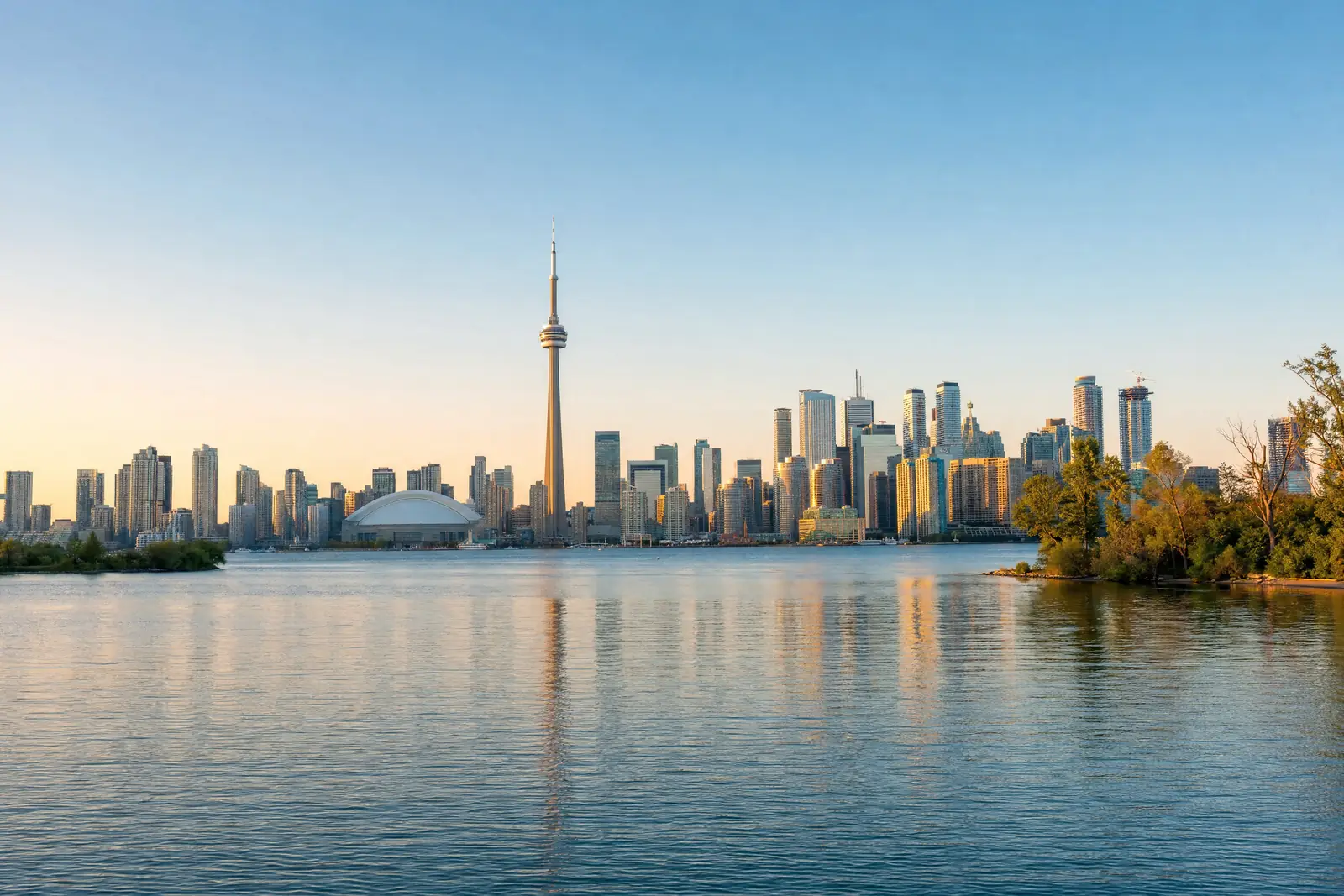 Toronto skyline with the CN Tower across calm lake water at sunset